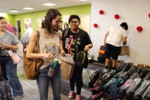 A teen and adult pick up school supplies from a stack.