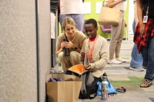 A teen holding backpack and a bag of schoolsupplies while their mentor looks on.