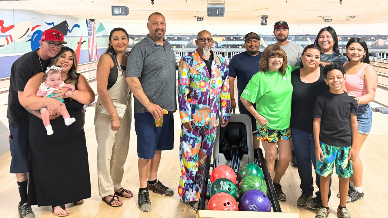 A group of smiling ARCA members and supporters stand together at the bowling alley, some holding bowling balls and others wearing event T-shirts, with colorful lanes and tournament signage in the background—capturing the spirit of community, fun, and heartfelt generosity that defines the annual charity event.